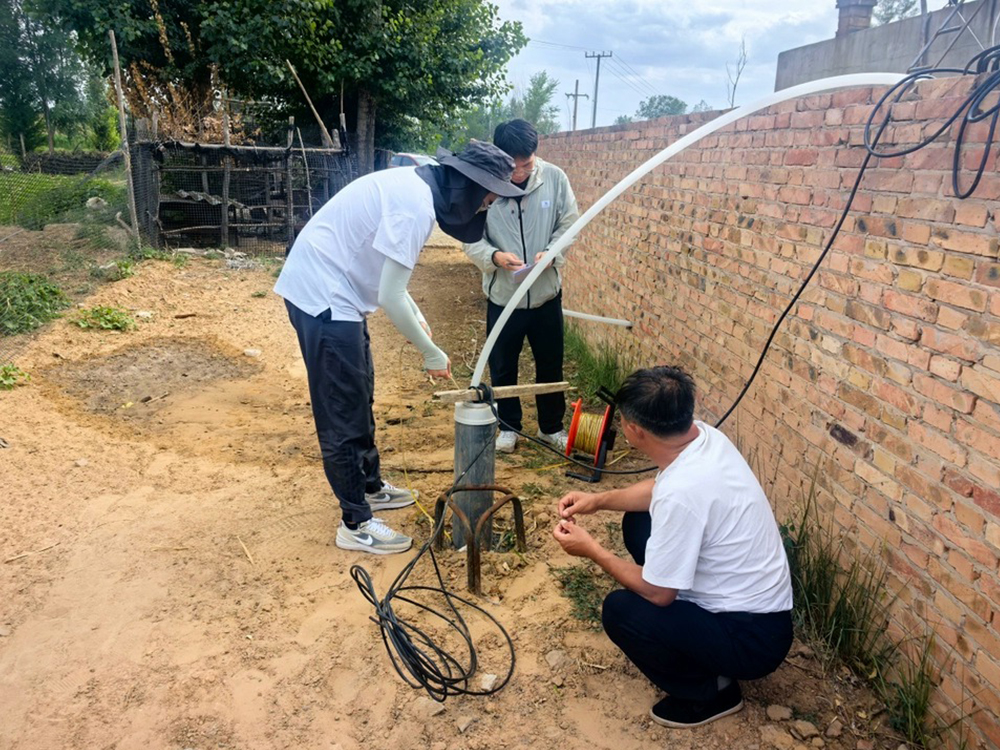 Technicians measuring groundwater level using a reel-type water level meter at a well site