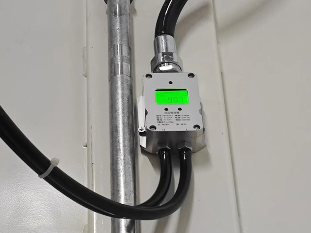Transmisor de presión diferencial de pared con pantalla verde retroiluminada instalado en un sistema de conductos de calefacción, ventilación y aire acondicionado.
